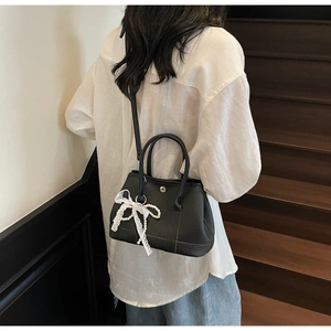 Detail of black lychee leather bucket bag featuring lace and pearl bow charm accessory