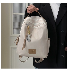 Detail of minimalist cream backpack with three zippers and a cute bear charm pendant