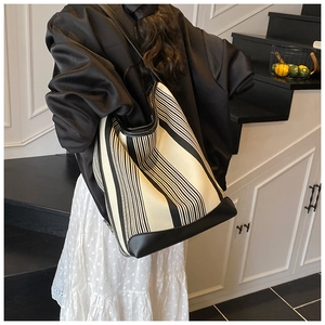 Detail of a large black and white striped canvas tote bag with black leather shoulder straps