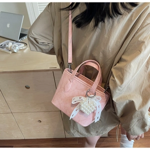 Dettaglio borsa rosa in pelle cerata con fiocco di pizzo e ciondolo di perle su legno