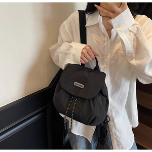 Detail of black nylon mini backpack featuring silver logo plaque and drawstring closure