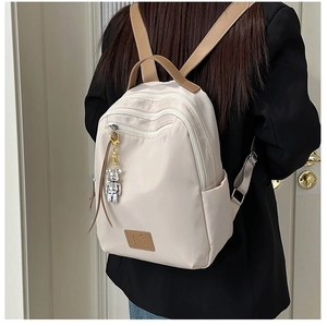 Detail of waterproof beige nylon backpack with brown straps and silver bear keychain