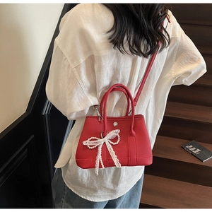 Detail of red lychee grain leather bucket bag with white lace bow and pearl chain deco