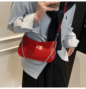 Detail of red glossy crescent shoulder bag with silver chain strap on striped shirt