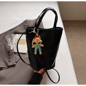 Détail d'un sac seau en cuir noir avec une breloque poupée sur un lit blanc