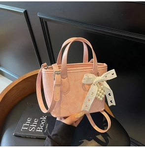 Dettaglio della borsa tote rosa con fiocco in pizzo e pendente di perle su una sedia
