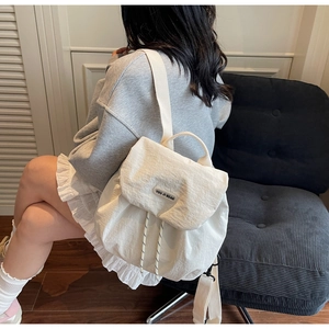 Detail view of white drawstring backpack with brand label on a soft grey textured sofa