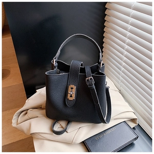 Dettaglio borsa a secchiello in pelle nera con chiusura a scatto su un trench beige