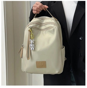 Close-up of beige waterproof nylon backpack featuring multi-zipper layers and bear charm