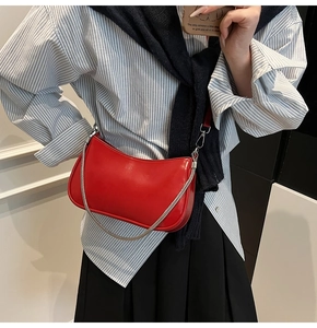 Close-up of red glossy semi-circular underarm bag with silver chain on model