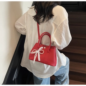 Lifestyle view of red textured bucket bag with lace bow accessory on stairs