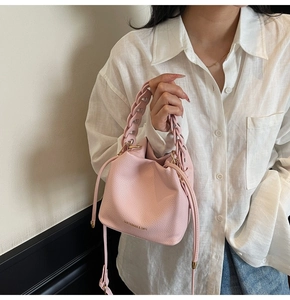 Detail of pink bucket bag featuring woven handle and pebbled leather texture on white shirt