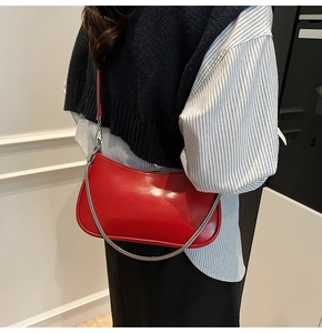 Detail of red crescent shoulder bag featuring silver metal chain and glossy leather texture