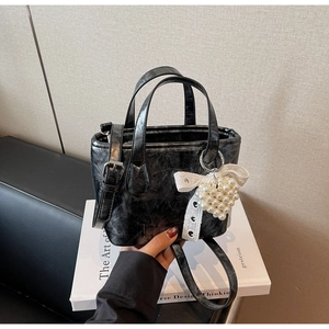 Dettaglio borsa a secchiello nera con texture retrò e ciondolo con perle e pizzo