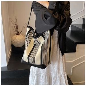 Detail of a large striped knit tote bag with black leather trim worn on the shoulder