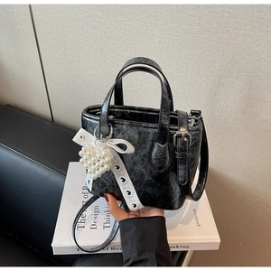Dettaglio della borsa nera con fiocco bianco e cuore di perla su pelle testurizzata