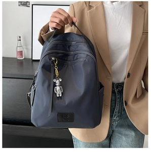 Detail of navy nylon backpack with multi-layer zippers and silver bear pendant