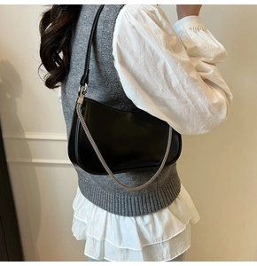 Detail of black leather underarm bag with silver chain strap on a stylish model