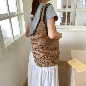 Close-up of handmade straw tote bag featuring contrast black straps and openwork weave