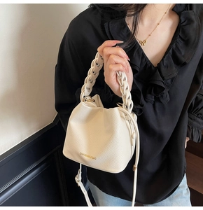 Close-up of white bucket bag featuring woven handle and gold branding on pebbled leather