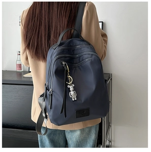 Detail of waterproof navy nylon backpack with silver zippers and a cute bear keychain