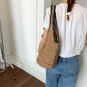 Detailed macro view of woven straw shoulder bag with black trim and natural raffia texture