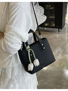 Minimalist black leather bucket bag with white tulip charm and crossbody strap on model