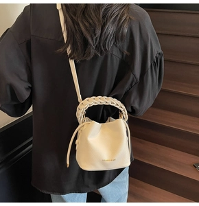 Rear view of model carrying a cream bucket bag with woven handle on wooden stairs