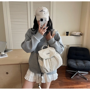 Detail of cream canvas backpack with drawstring closure and brand flap shown on model