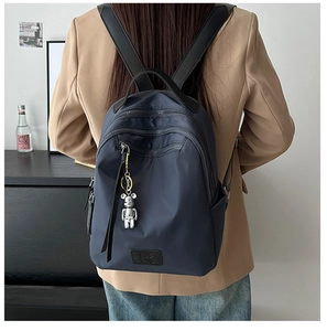 Detail of navy nylon backpack with multi-zipper layers and silver bear keychain charm