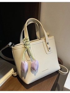 Chic cream leather bucket bag with tulip charm and crossbody strap on a wooden surface