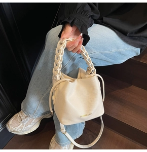 Detail of cream bucket bag featuring lychee texture and woven handle held by model