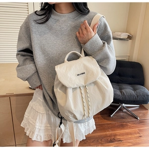 Detail of cream canvas backpack with drawstring closure and brand label on model