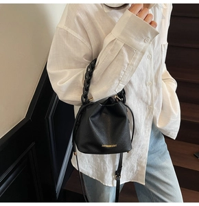 Detail of black pebbled leather bucket bag with gold logo and woven chain handle
