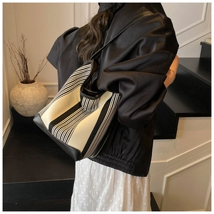 Minimalist black and white striped canvas tote with leather base shown on shoulder