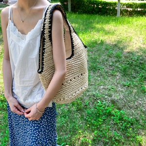 Detail of hand-woven straw tote bag with black crochet trim and geometric cutout patterns