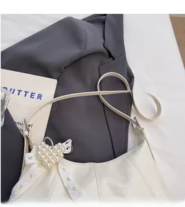 Close-up of a white leather underarm bag with pearl heart pendant and lace bow detail