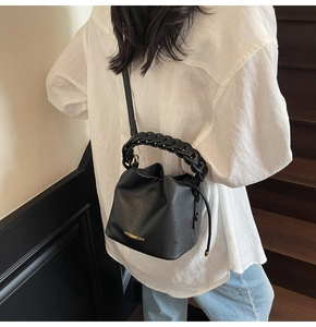 Detail of black pebbled leather bucket bag featuring a woven chain handle and gold logo
