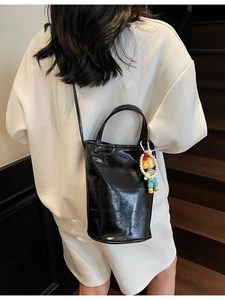Sac seau noir minimaliste avec charme de poupée, porté par un mannequin sur un escalier