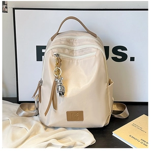 Detail of cream travel backpack showing multiple zipper pockets and metal bear pendant