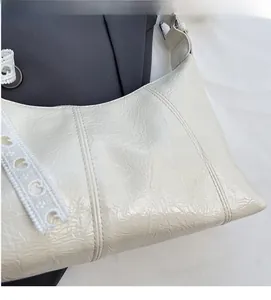 Detail of white pleated underarm bag featuring lace strap with G-letter embroidery