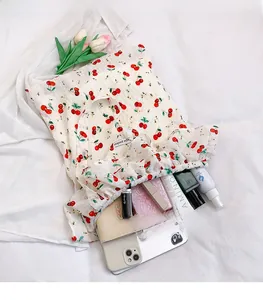 Detail of cream canvas tote bag with red cherry prints and ruffled edge design
