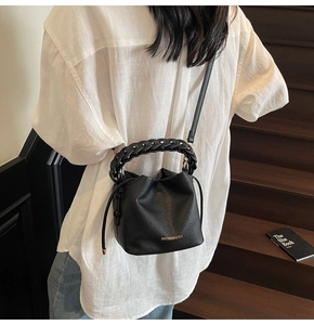 Detail of black lychee grain leather bucket bag featuring gold logo and woven handle