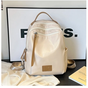Close-up of cream nylon travel backpack featuring front zipper pocket and leather logo patch
