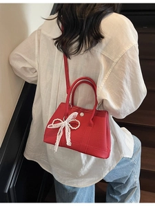 Red pebbled leather bucket bag with lace bow and pearl charm shown on model