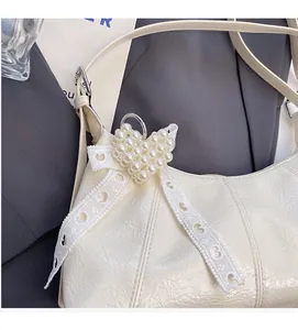 Detail of cream leather shoulder bag featuring heart pearl charm and white lace bow