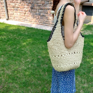 Detail of hand-woven straw hobo bag with cream texture and black decorative stitching