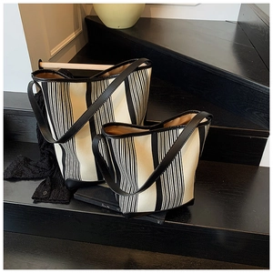Detail of two striped canvas tote bags with black leather trim on a modern staircase
