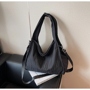 Detail of black pleated fabric underarm bag with adjustable straps on a textured leather sofa