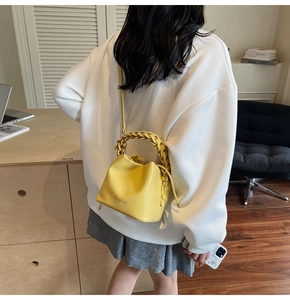 Bright yellow bucket bag in lychee leather featuring a woven handle and long shoulder strap